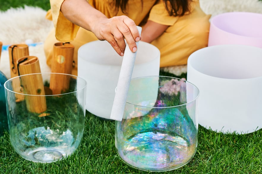 Woman playing music on crystal singing bowls, relaxing in beautiful green garden